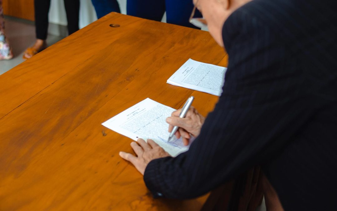 Firma de un acuerdo de colaboración profesional entre representantes institucionales en una mesa de reuniones.